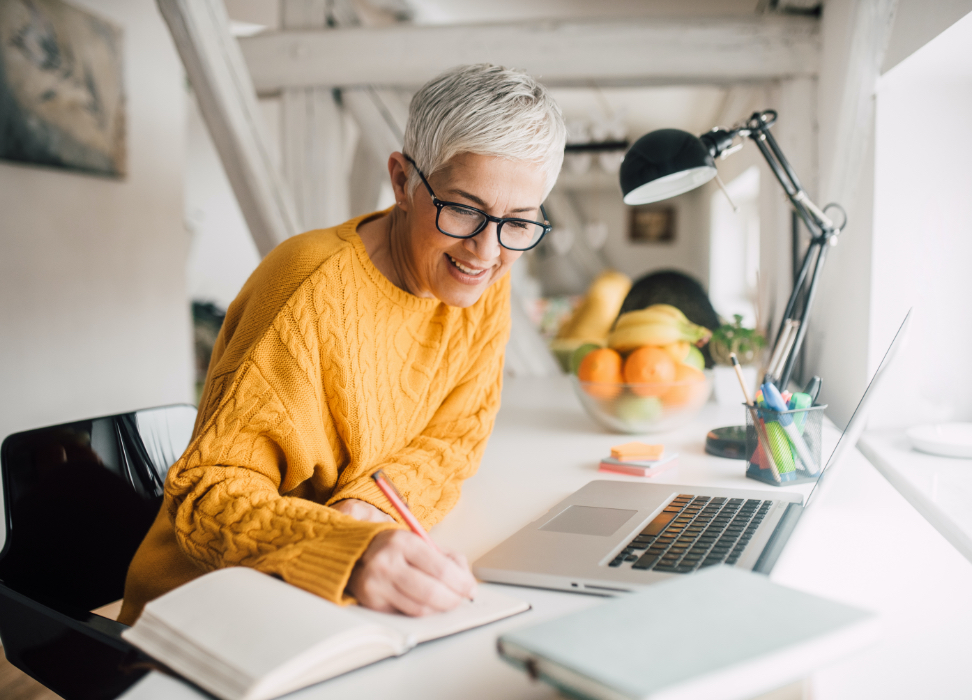 Mature woman sitting at desk writing in notebook.