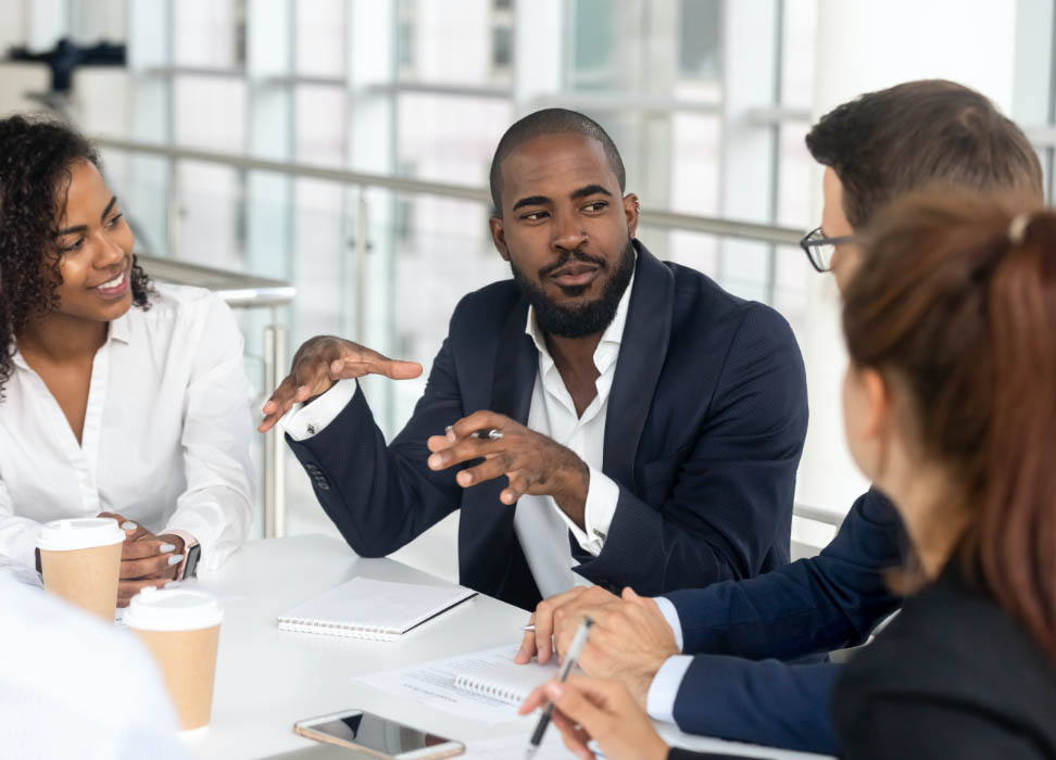 businessman speaking with people at table in office.