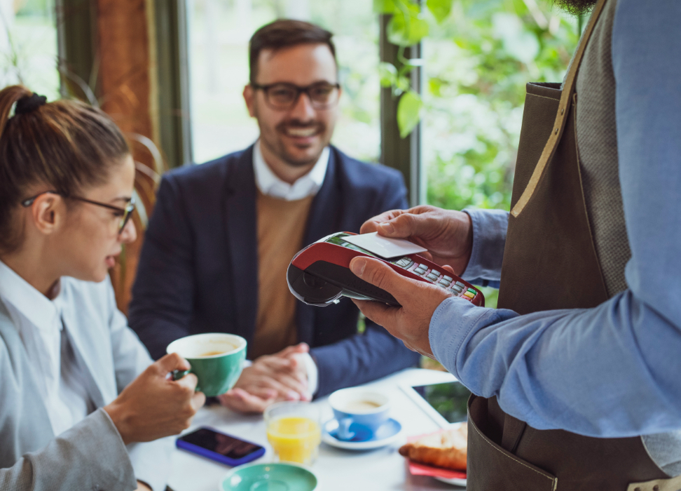 Man and woman sitting at table in restaurant paying for meal with card.