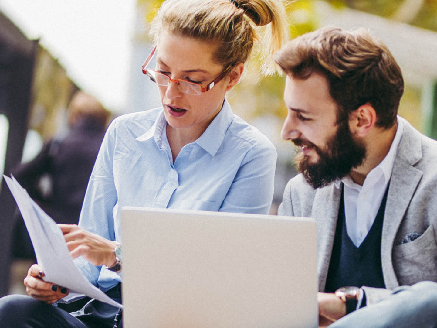 Man and woman sitting outside with laptop reviewing paperwork.