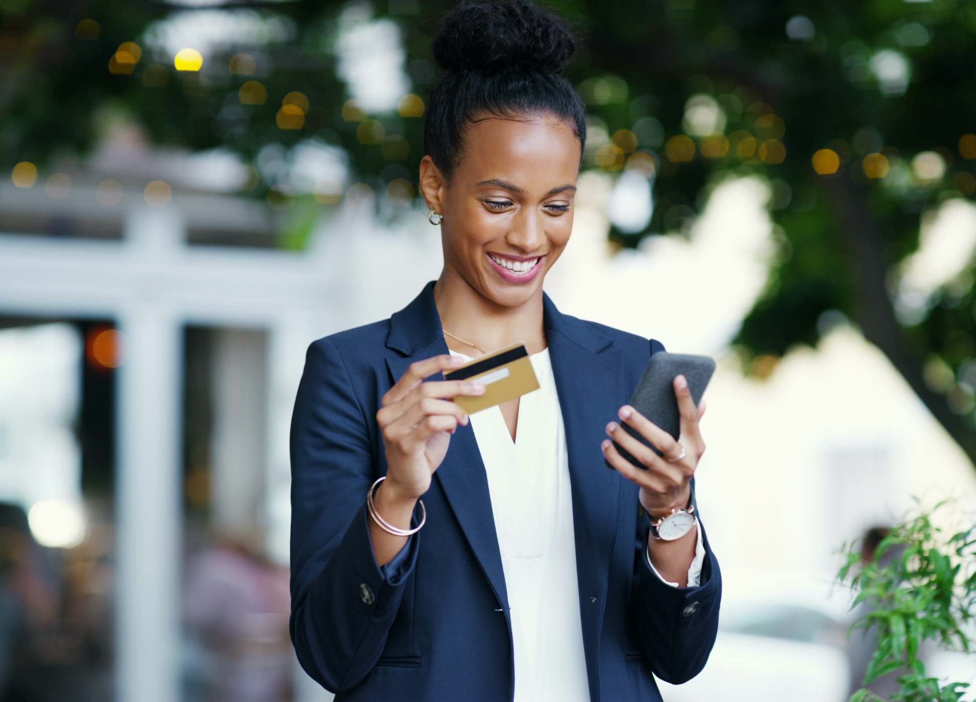 Woman standing outside of building holding mobile device and debit card.