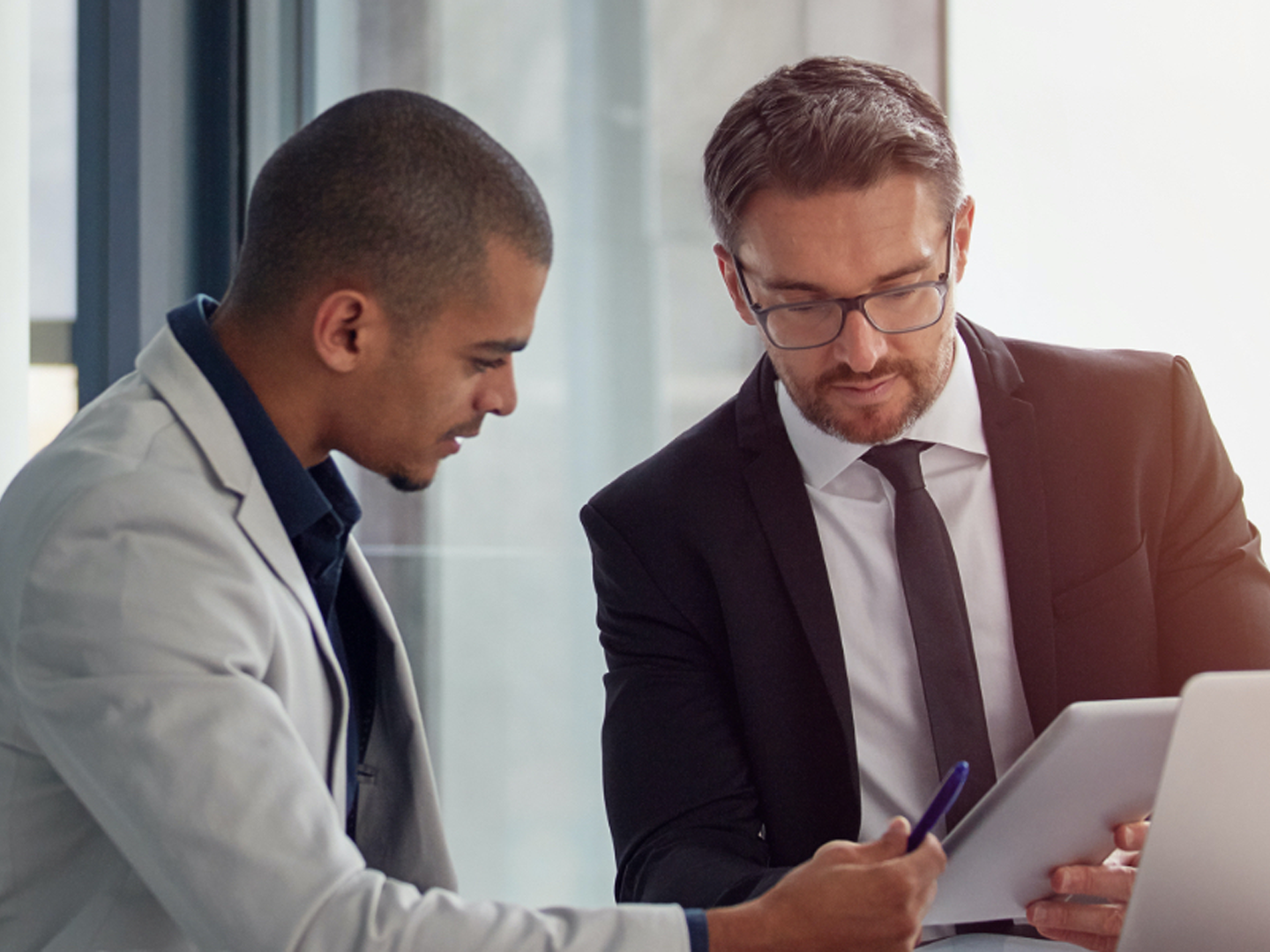 Two men in business attire looking at tablet.