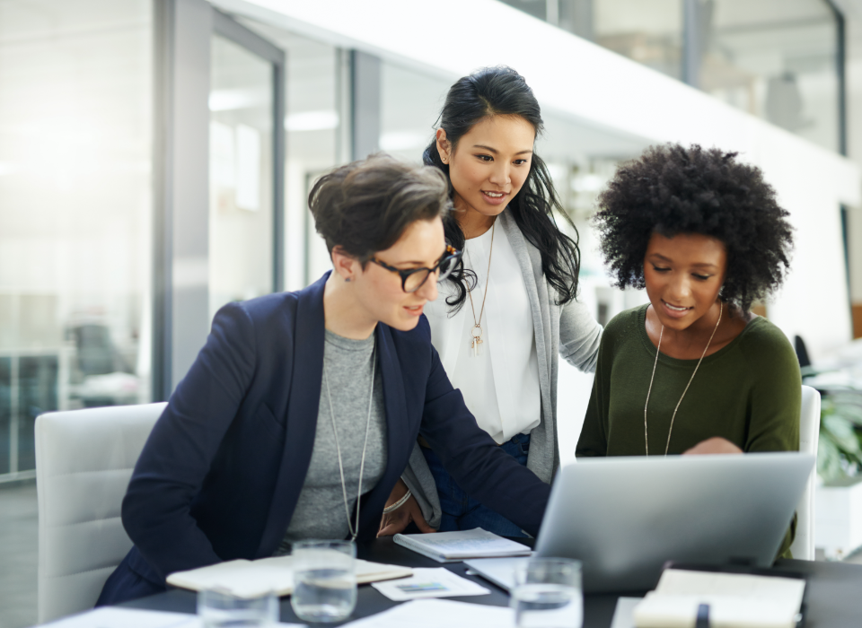 Three women in office looking at laptop computer.