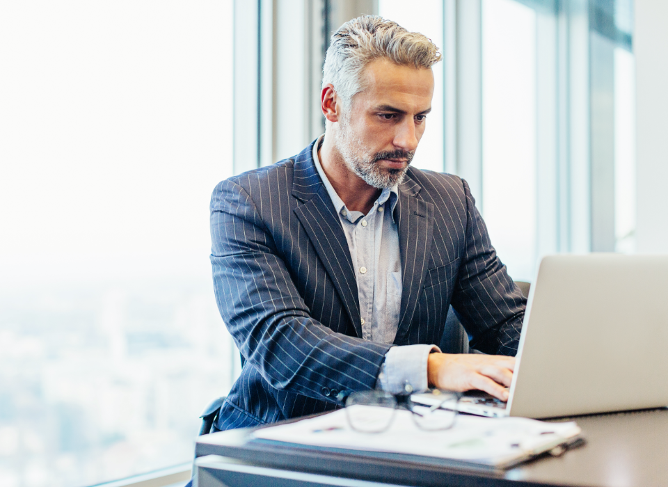 Man wearing striped jacket sitting at table looking at laptop.