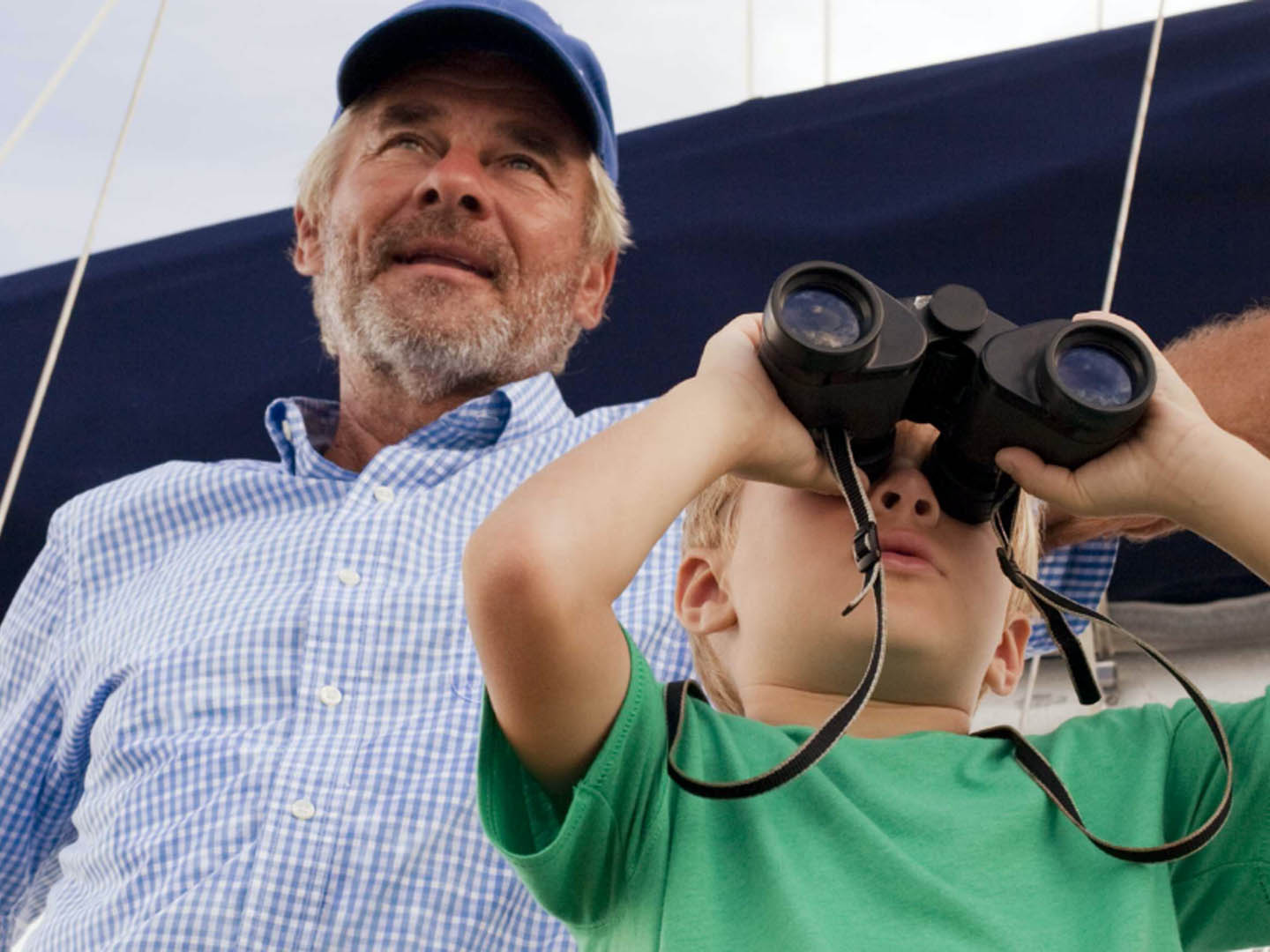 Man wearing hat and boy looking through binoculars standing on sailboat