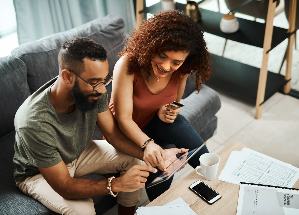 Man and woman sitting on couch looking at bank account on tablet.