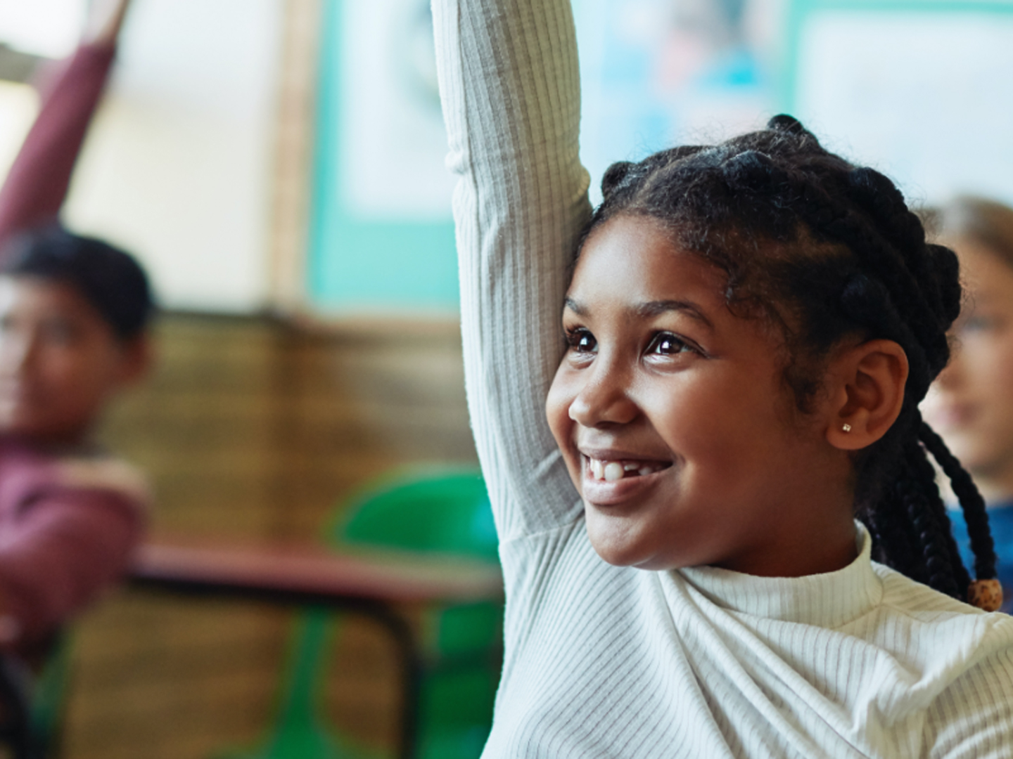 Girl in classroom smiling with raised hand.