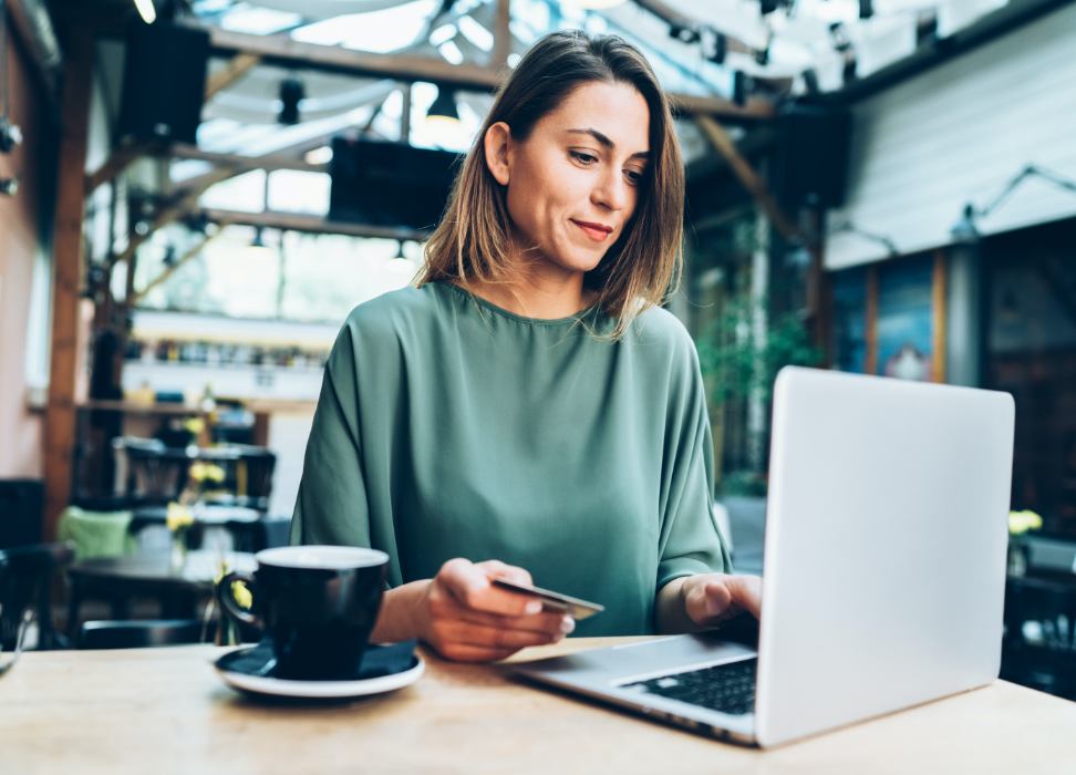 Woman sittng at table with cup and laptop wearing a green shirt.