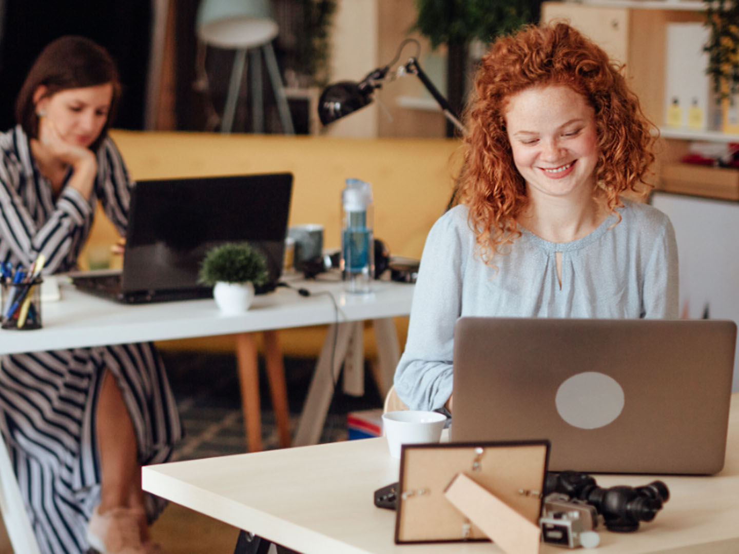 Two women sitting at desks looking at laptops.