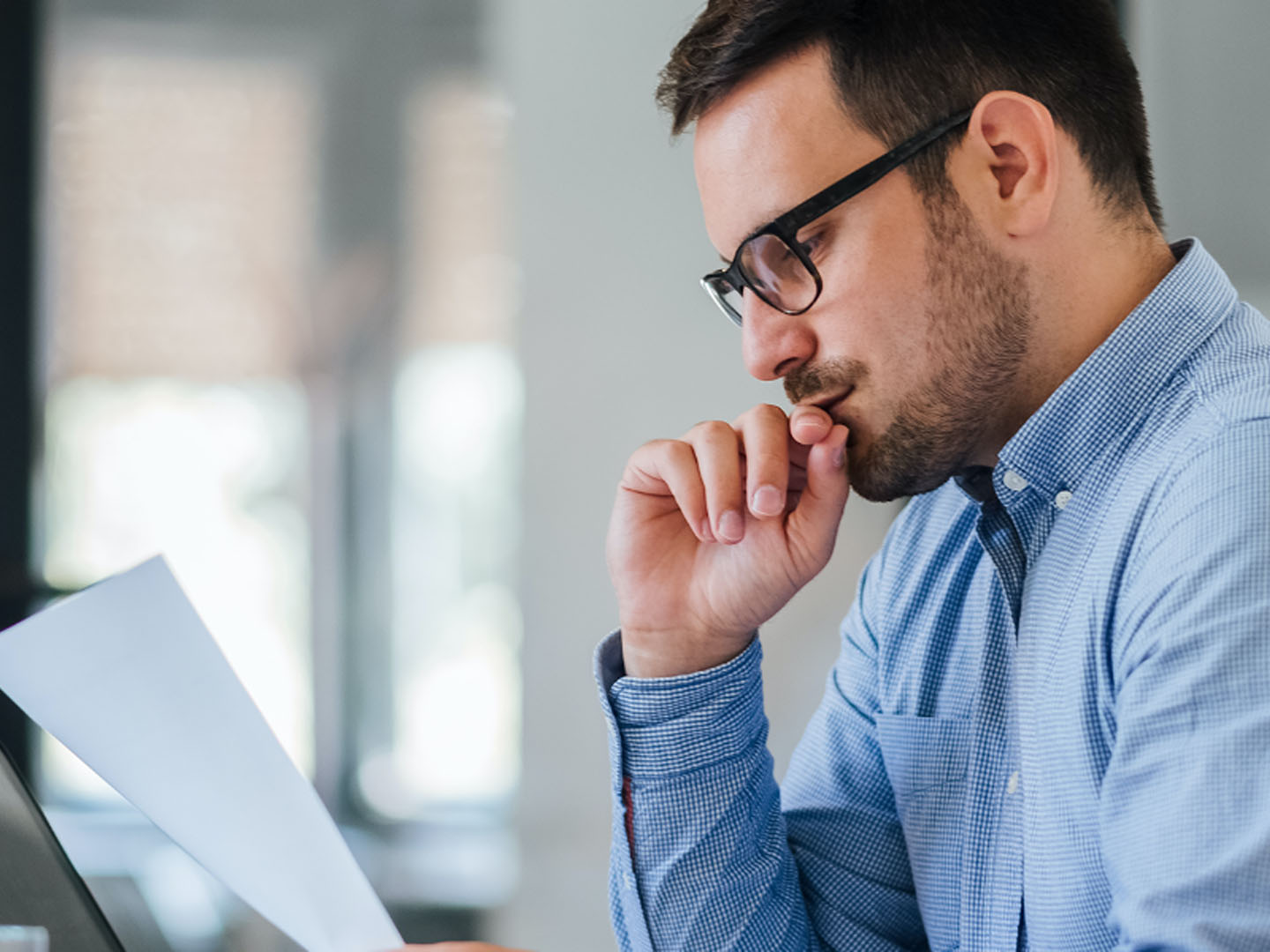 Man sitting with hand to mouth looking at paper.