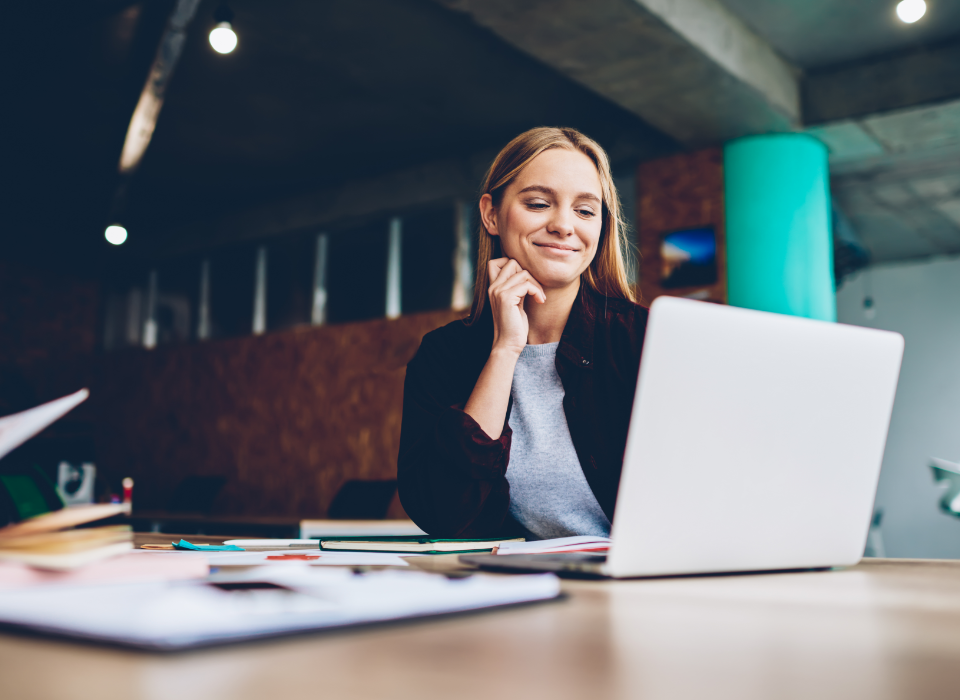 Woman sitting at table smiling while looking at laptop.