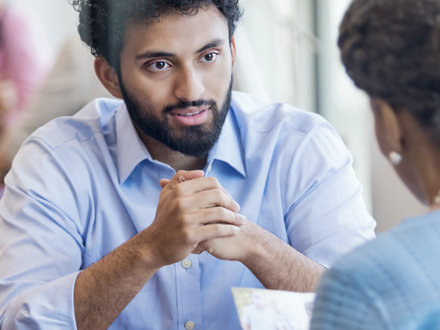 Man in blue shirt sitting at table speaking to woman.