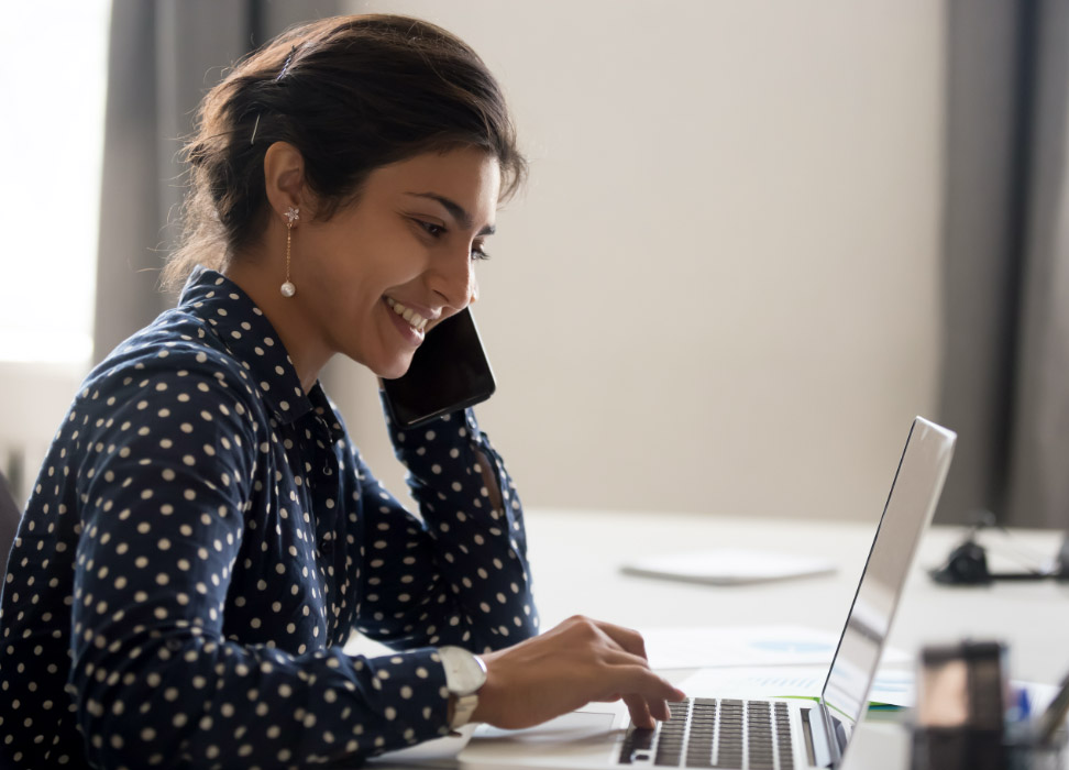 Woman sitting at desk wearing polka dot shirt looking at laptop.
