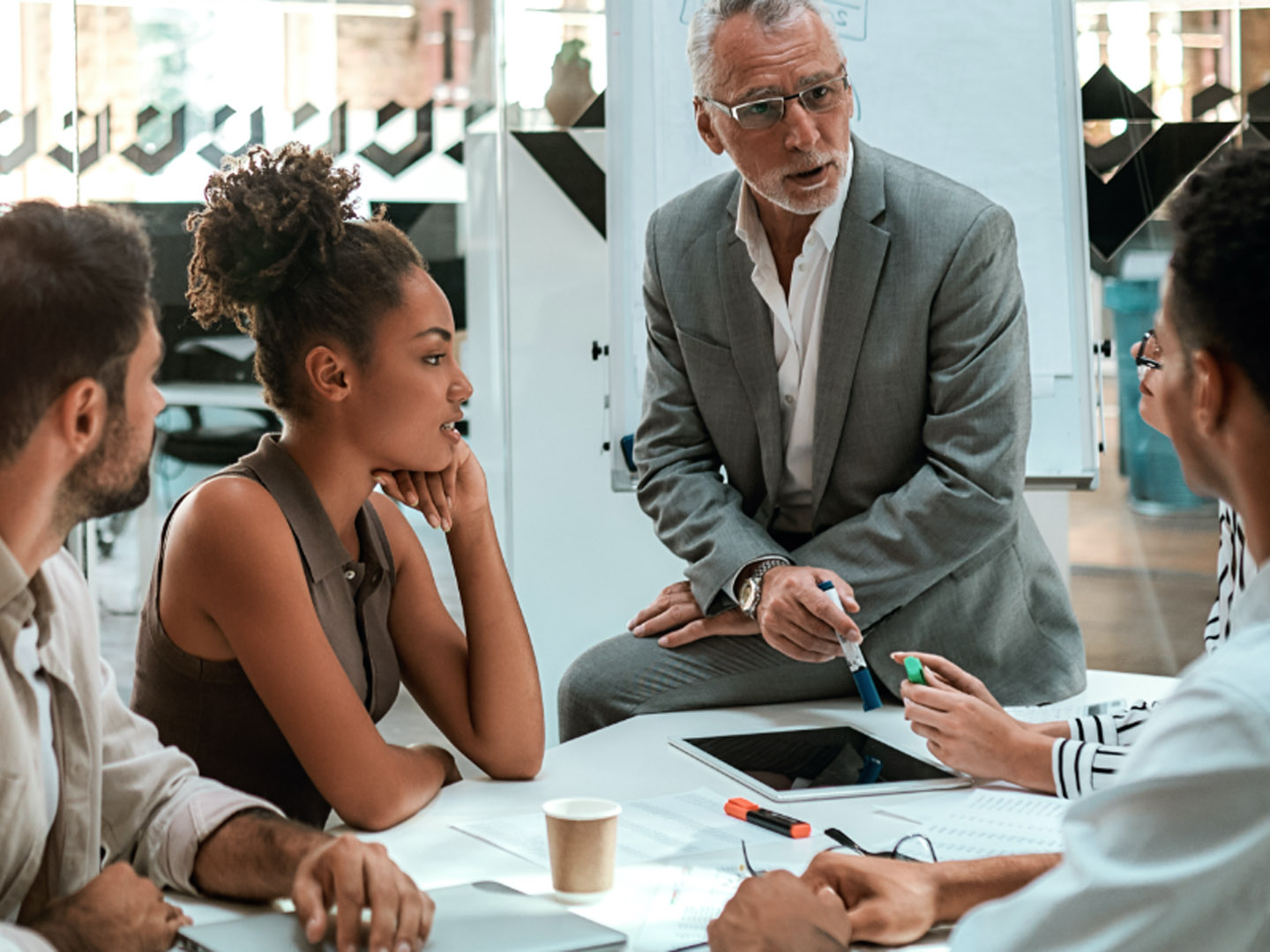 Man sitting on table speaking to a group of people in office.