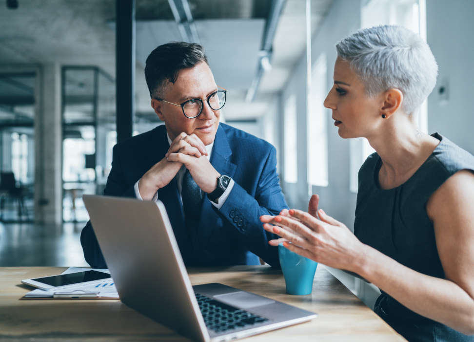 Businesswoman and businessman sitting at table with laptop talking.