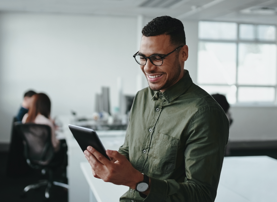 Man wearing glasses standing and looking at tablet.