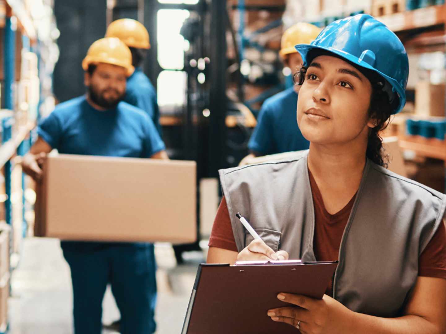 Woman wearing hard hat with clipboard and pen.