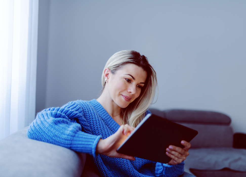Woman in blue sweater sitting on couch looking at tablet
