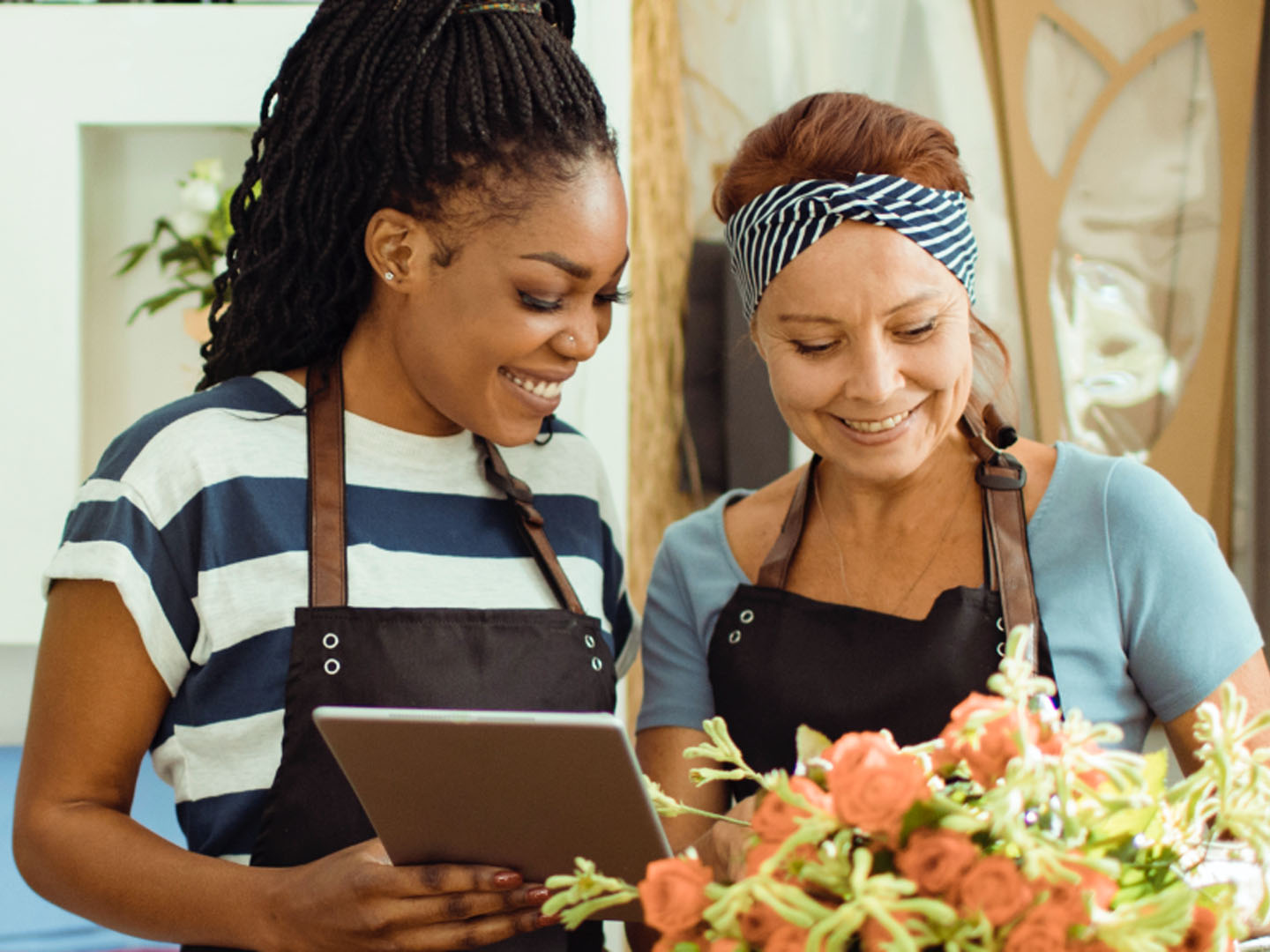 Two women wearing aprons looking at tablet.