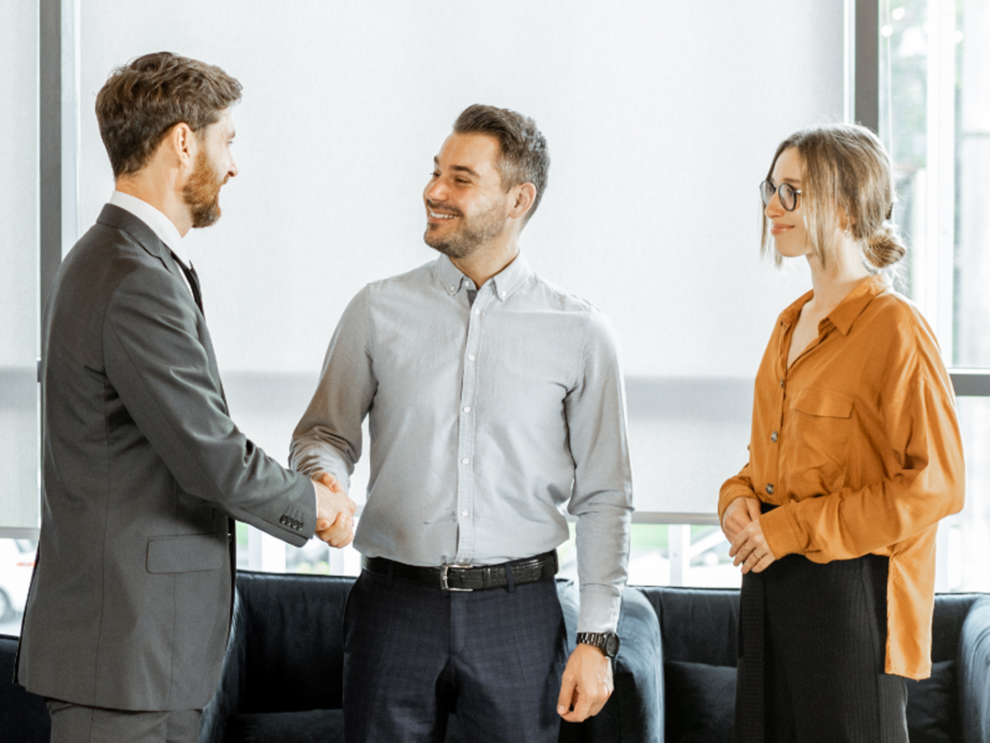 Two men and a woman standing in office shaking hands.