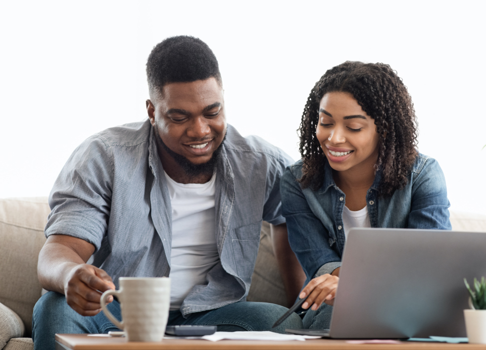 Man and woman sitting on couch reviewing paper with coffee and laptop.