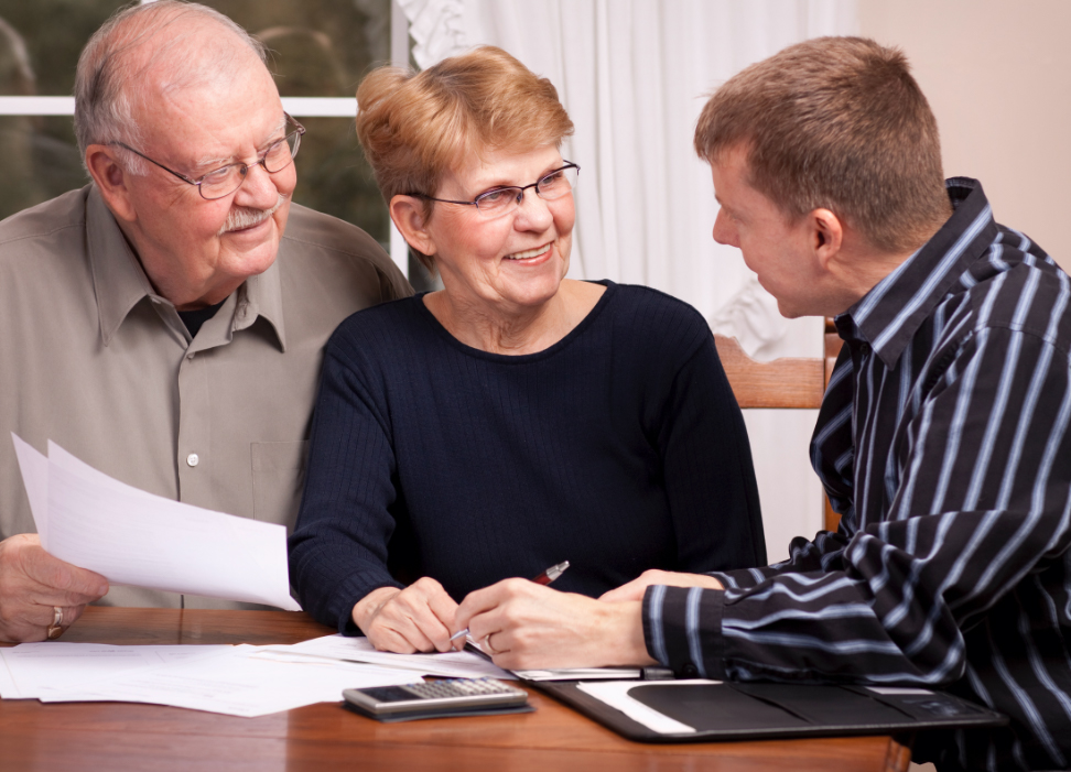 Senior citizen man and woman sitting at a table with consultant reviewing documents.