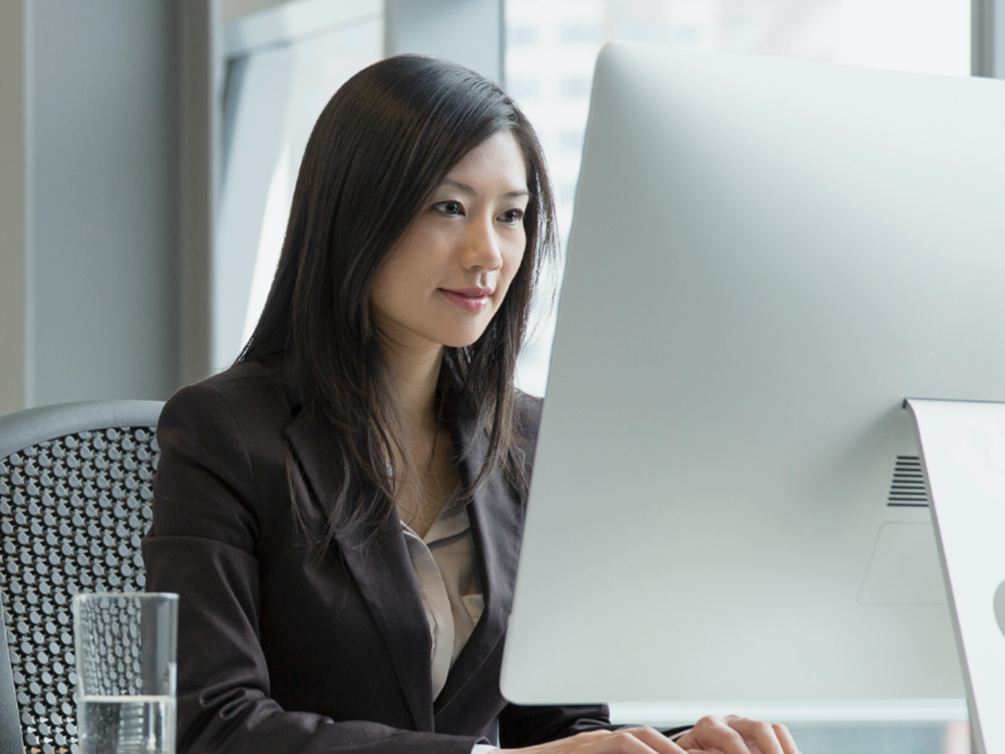 Woman sitting at desk looking at desktop computer.