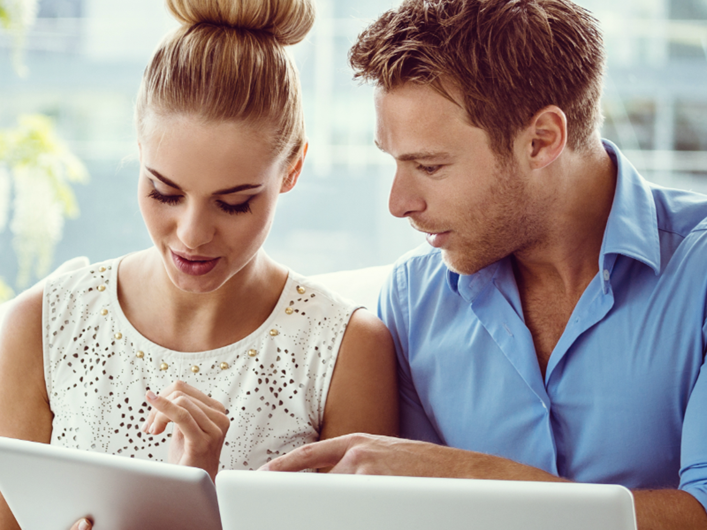 Man and woman sitting looking at tablet and laptop.