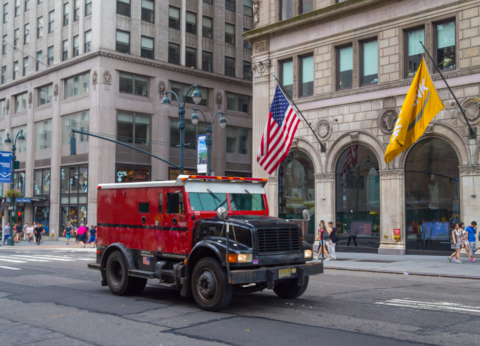 Red and black armored car driving down city street.