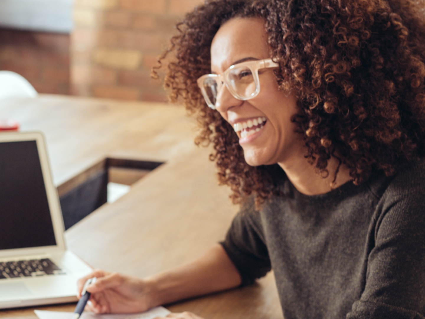 Woman wearing glasses sitting at desk laughing.