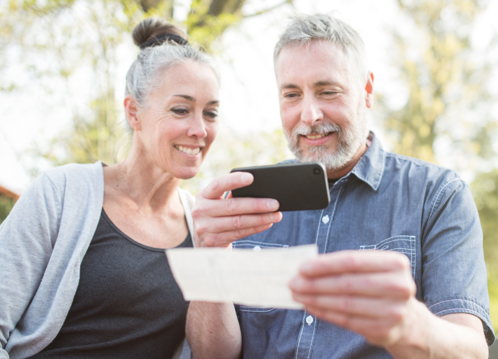 Mature man and woman depositing check with mobile phone.