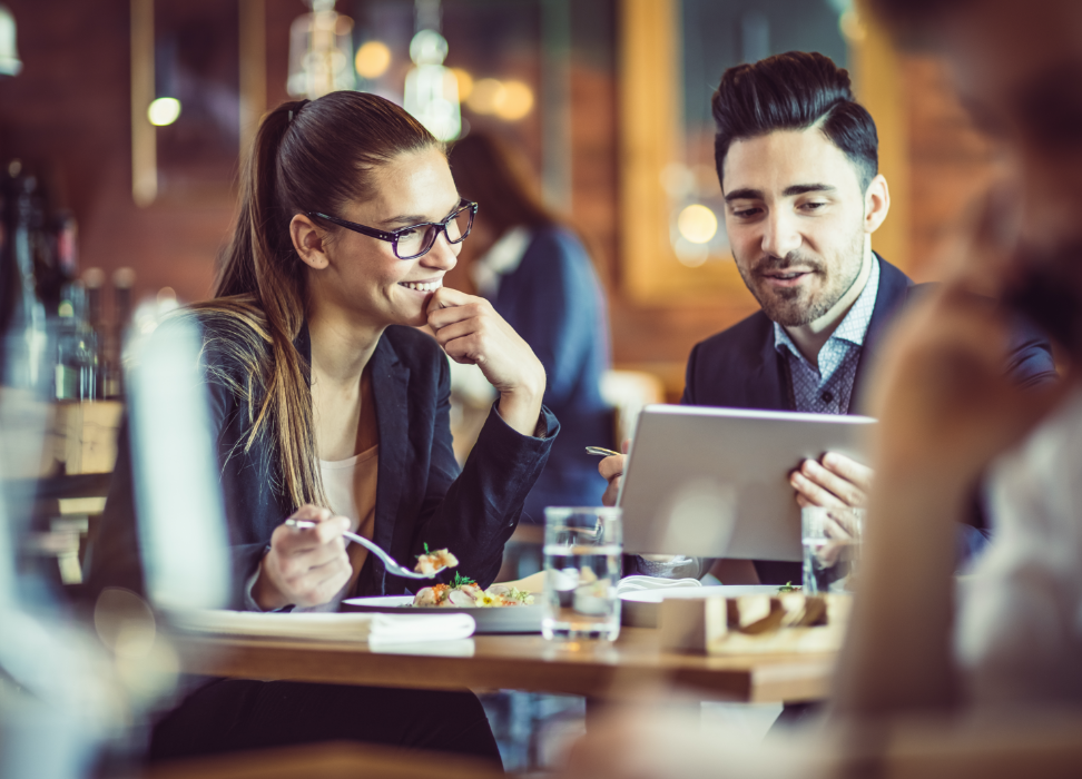 Man and woman sitting at table in restaurant looking at tablet.