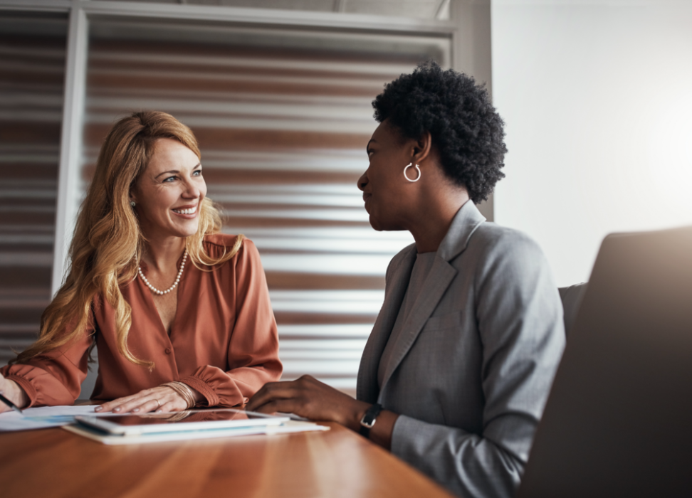 Two woman sitting at desk discussing commercial services.