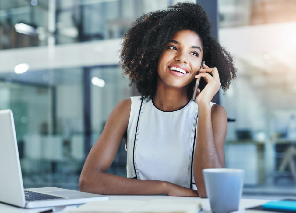 Woman sitting at desk talking on cell phone.