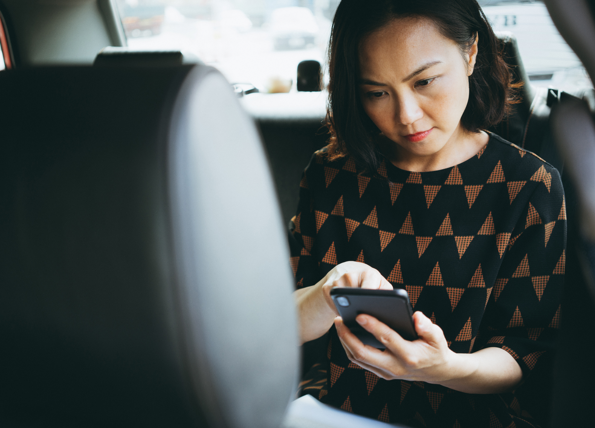 Woman sitting in back seat of car looking at mobile device.