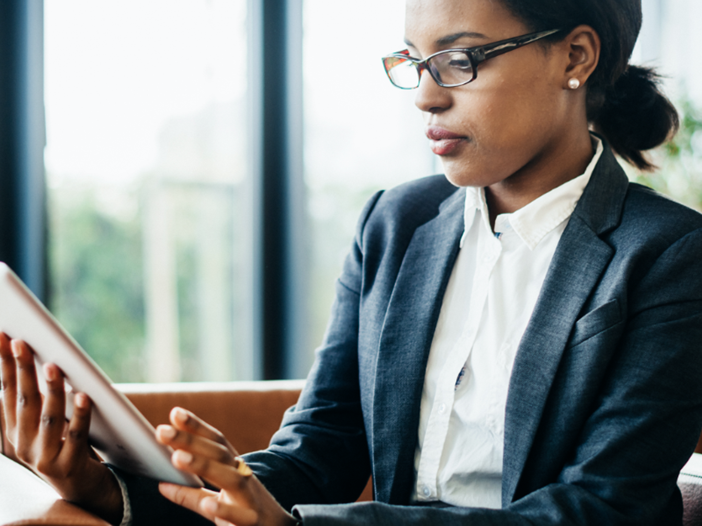 Woman wearing glasses sitting at table with tablet.