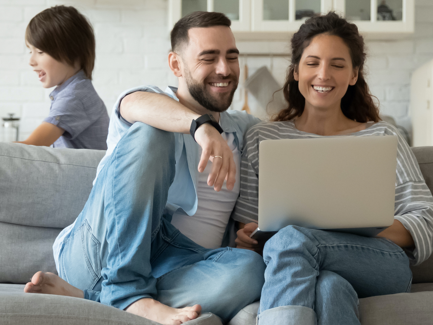 Man and woman sitting on couch wearing blue jeans with laptop.