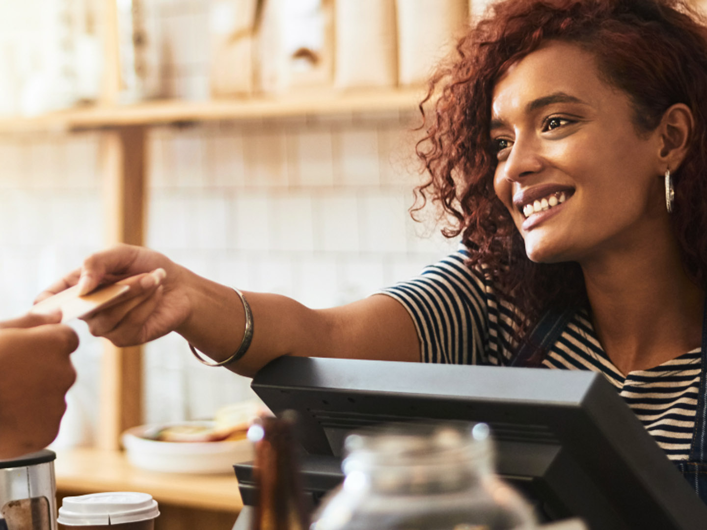 Woman merchant smiling while handing back credit card.