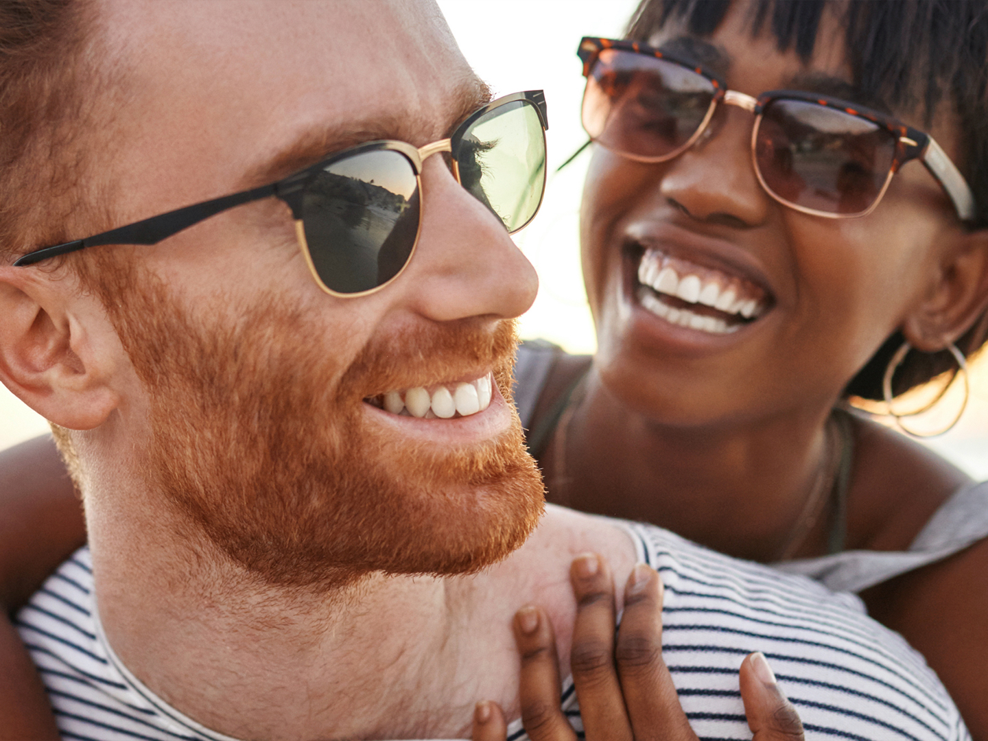 Woman with arms around a man smiling wearing sunglasses.