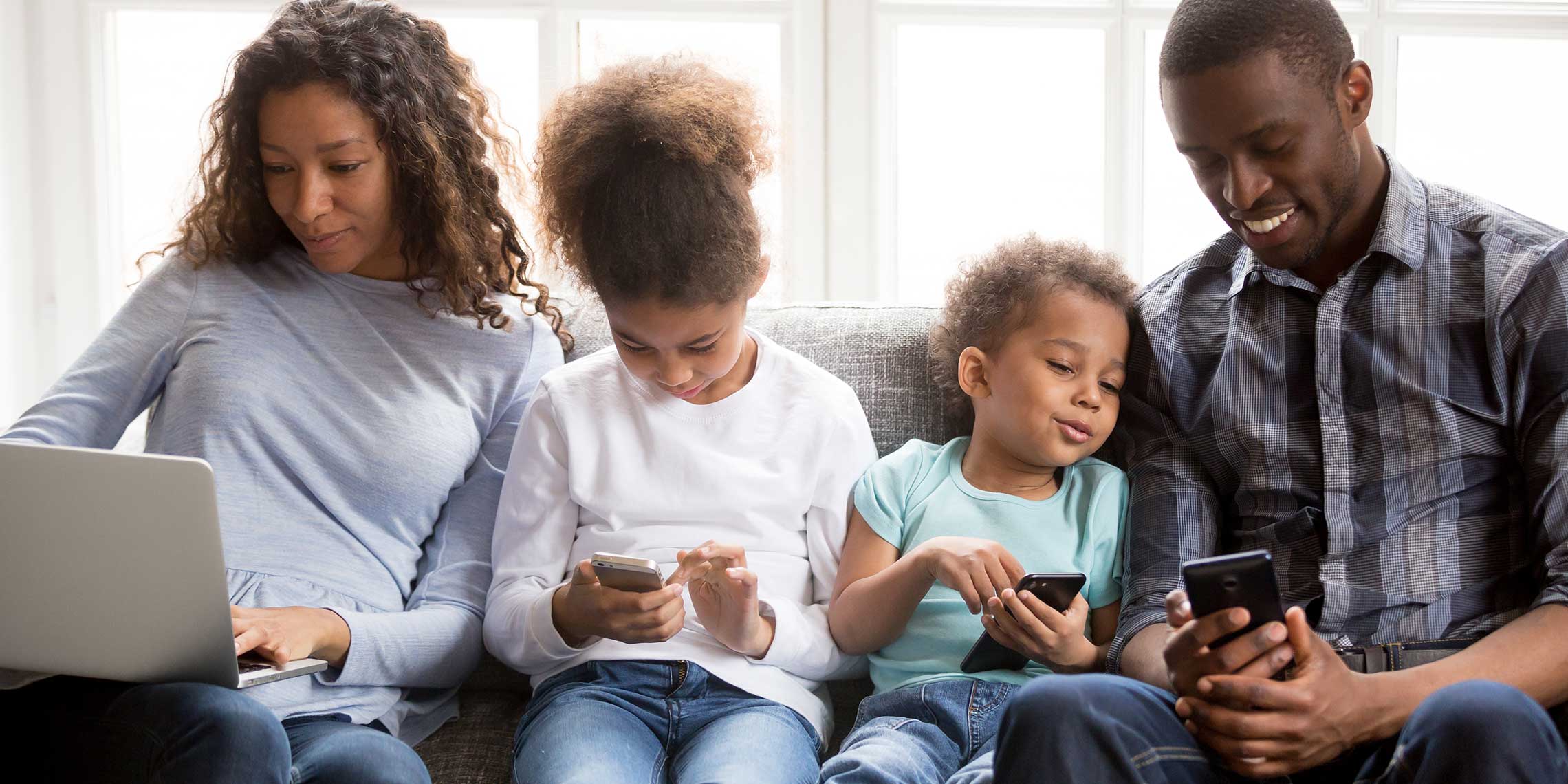 family sitting on the couch using laptops and cell phones