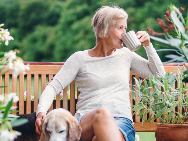 A person enjoying a cup of coffee in a garden while petter a dog