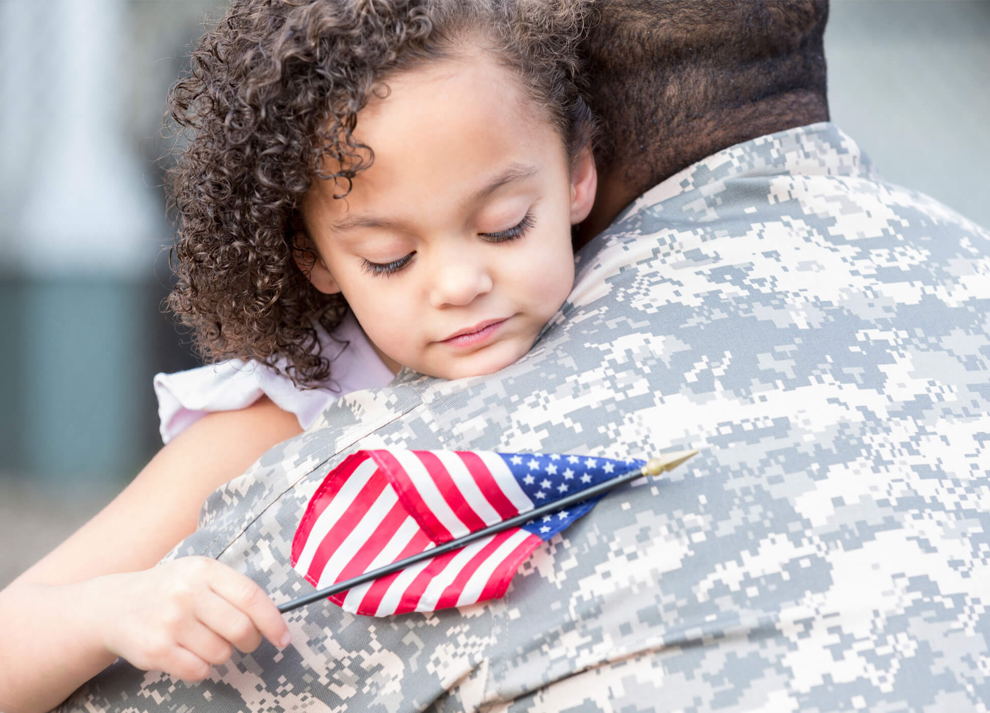young girl holding American flag hugging a military veteran