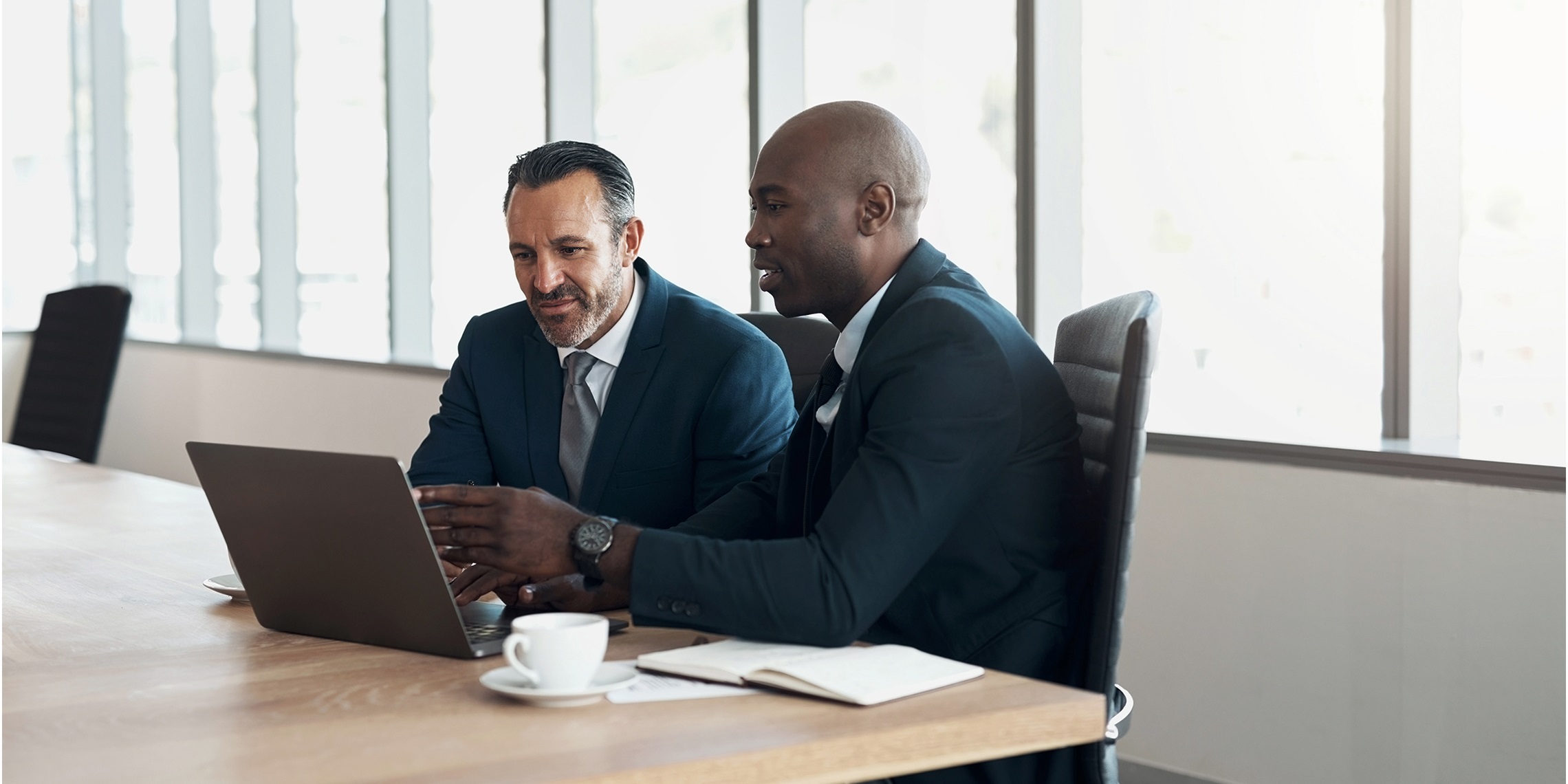 two men sitting in a conference room looking at laptop