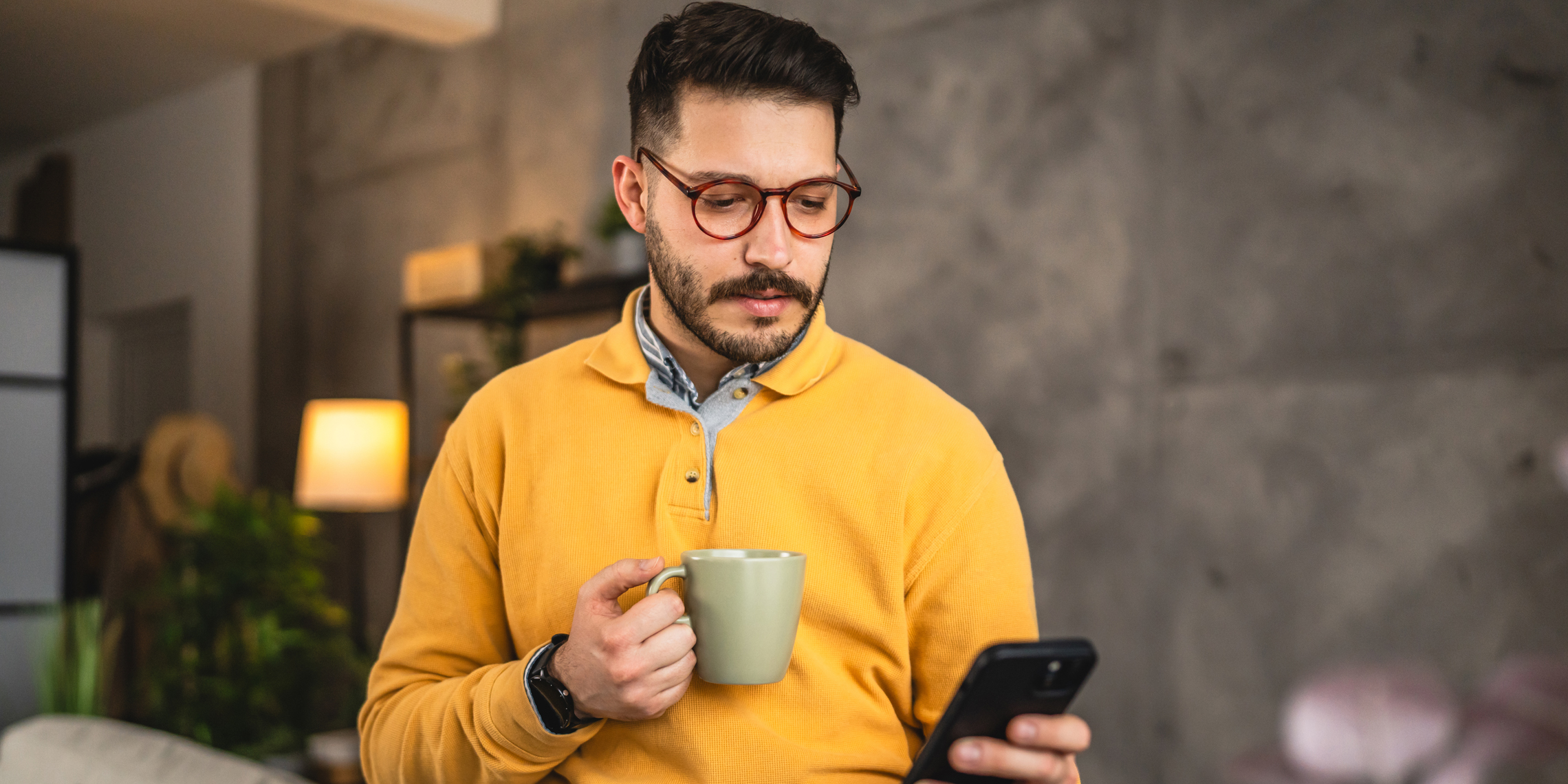 Man drinking coffee looking at phone.